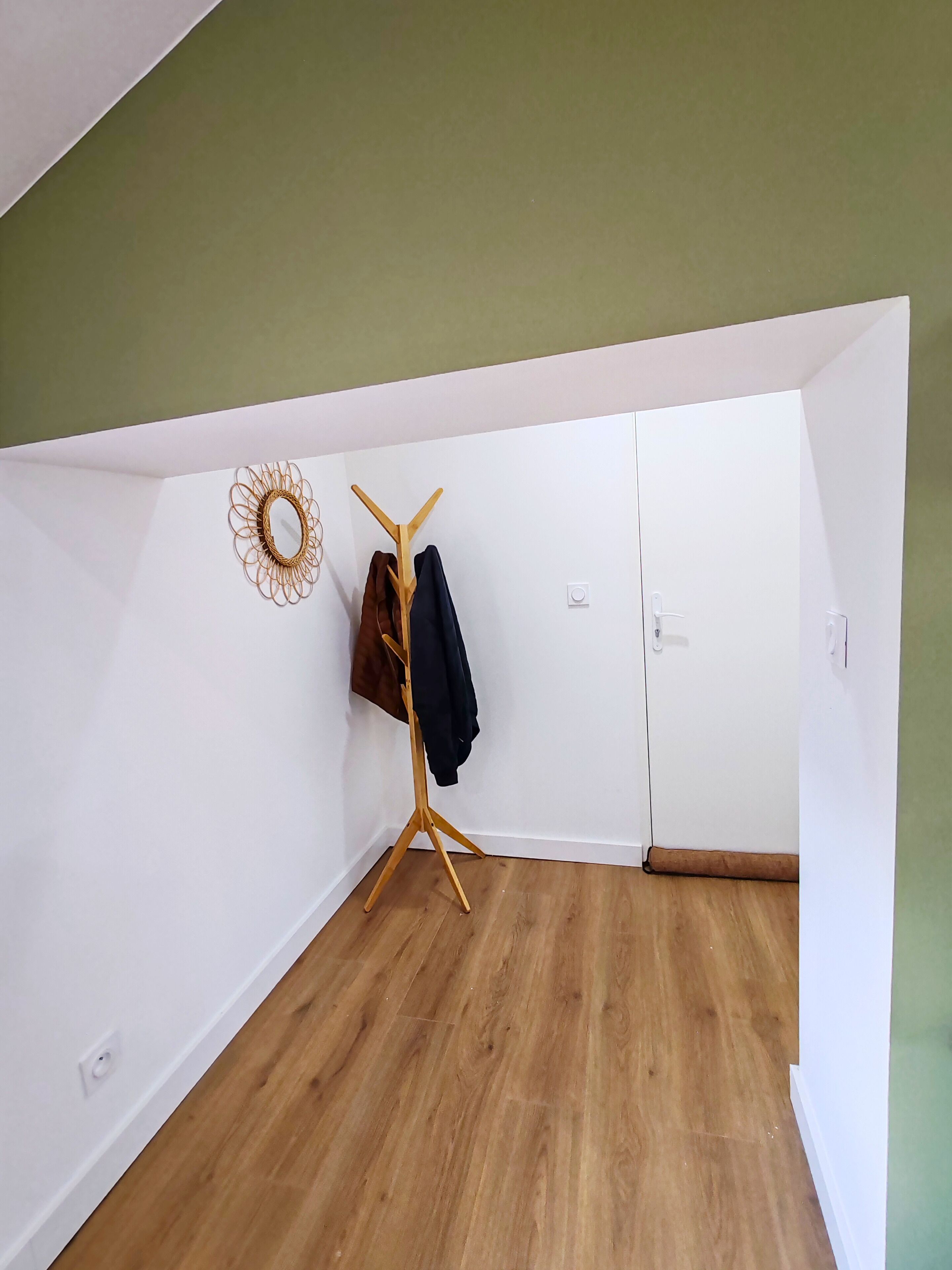 Ein Zimmer mit Holzboden, Kleiderhaken mit Kleidung, einer Tür und einer runden Wanddekoration.