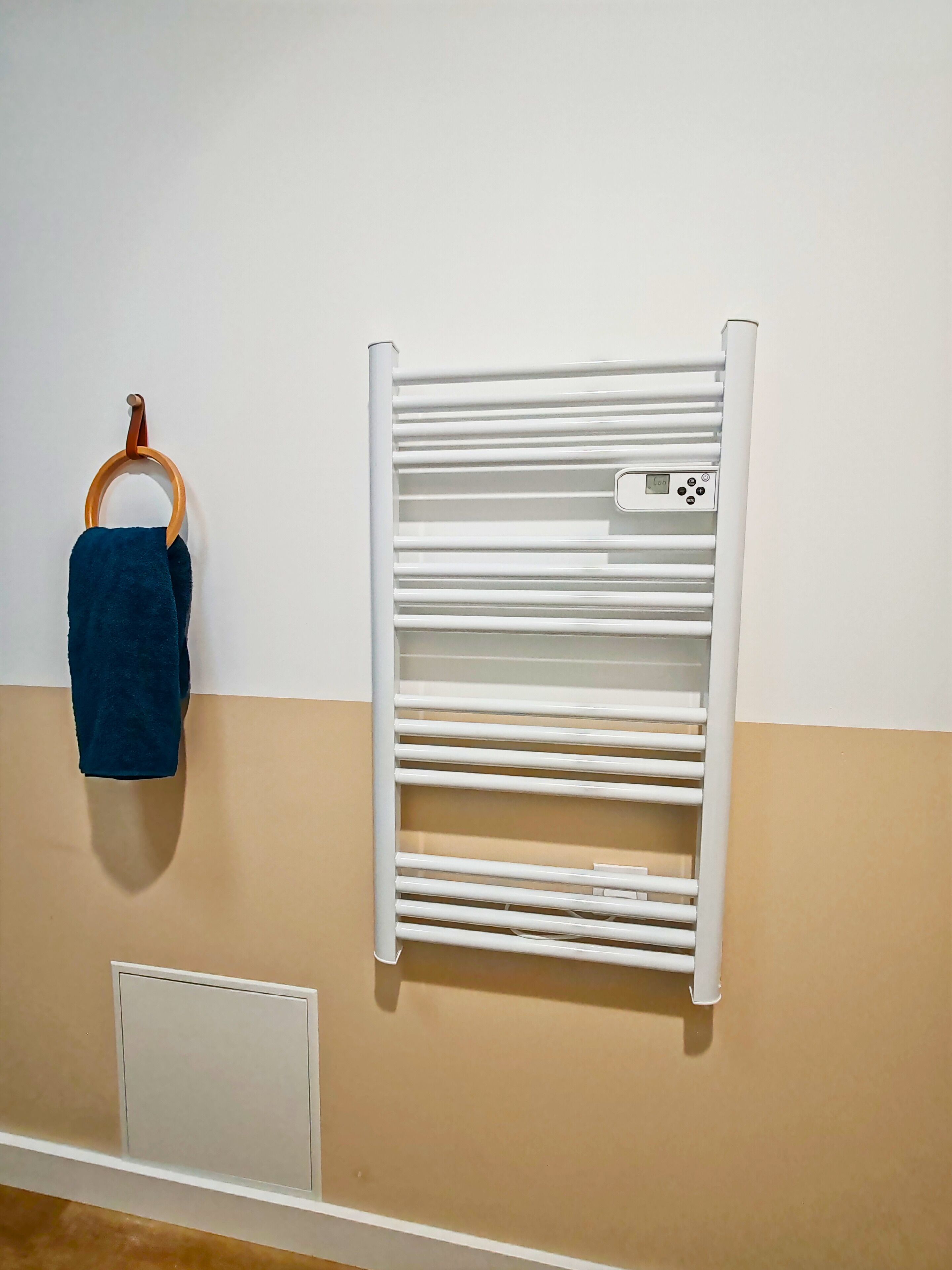 A towel rack with a blue towel hanging on it, a white towel heater, and a beige wall.