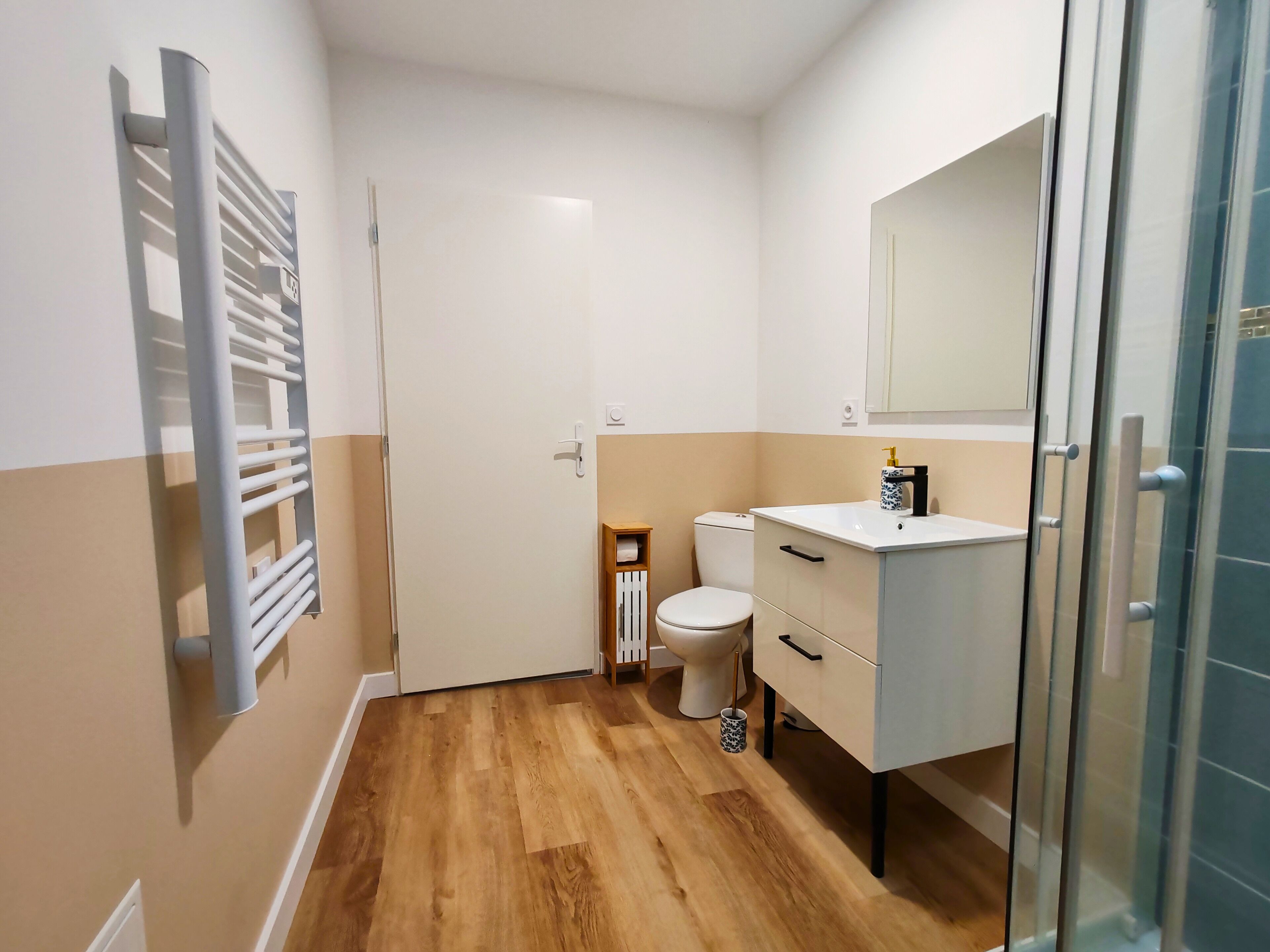 Une petite salle de bain avec un plancher en bois, un lavabo blanc, des toilettes et une cabine de douche en verre.