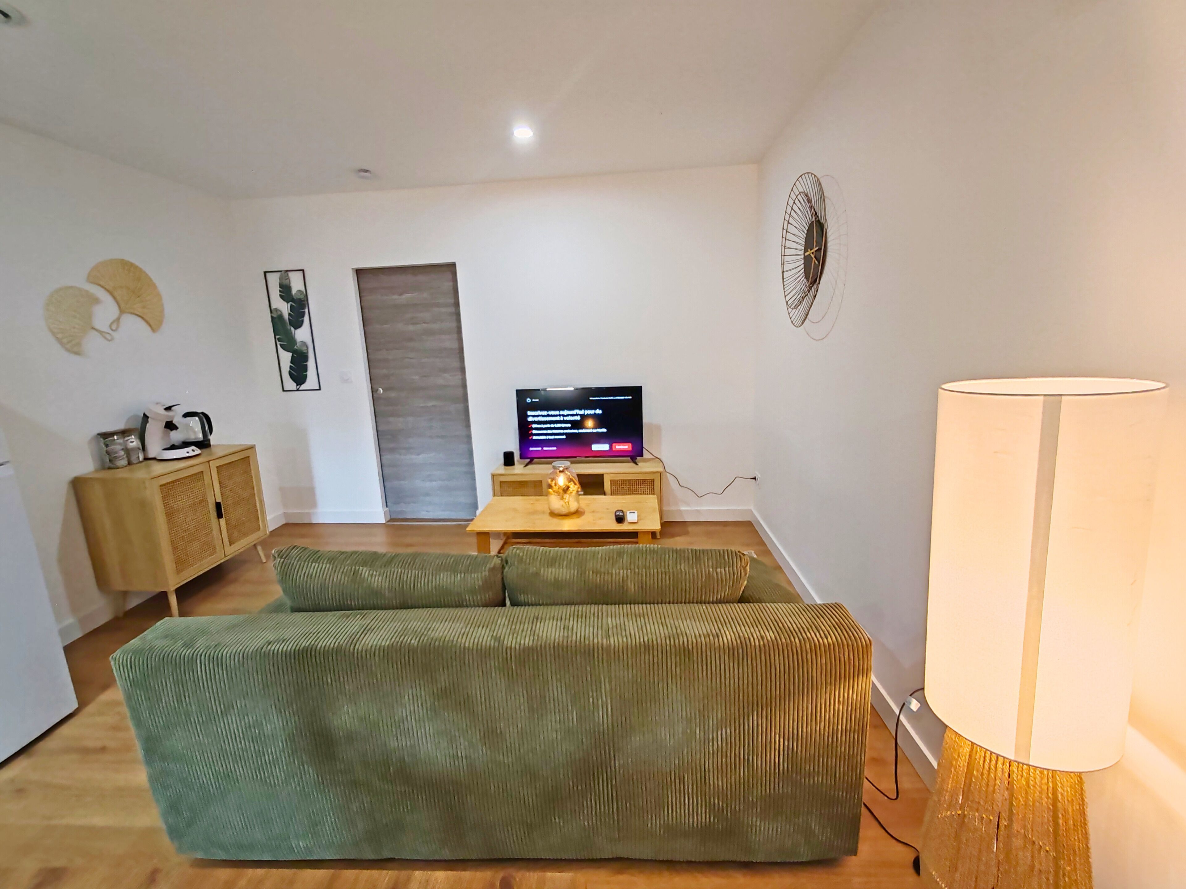 A living room with a green sofa, a wooden cabinet, a television, and a lamp.