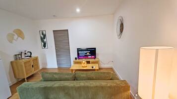 A living room with a green sofa, a wooden cabinet, a television, and a lamp.