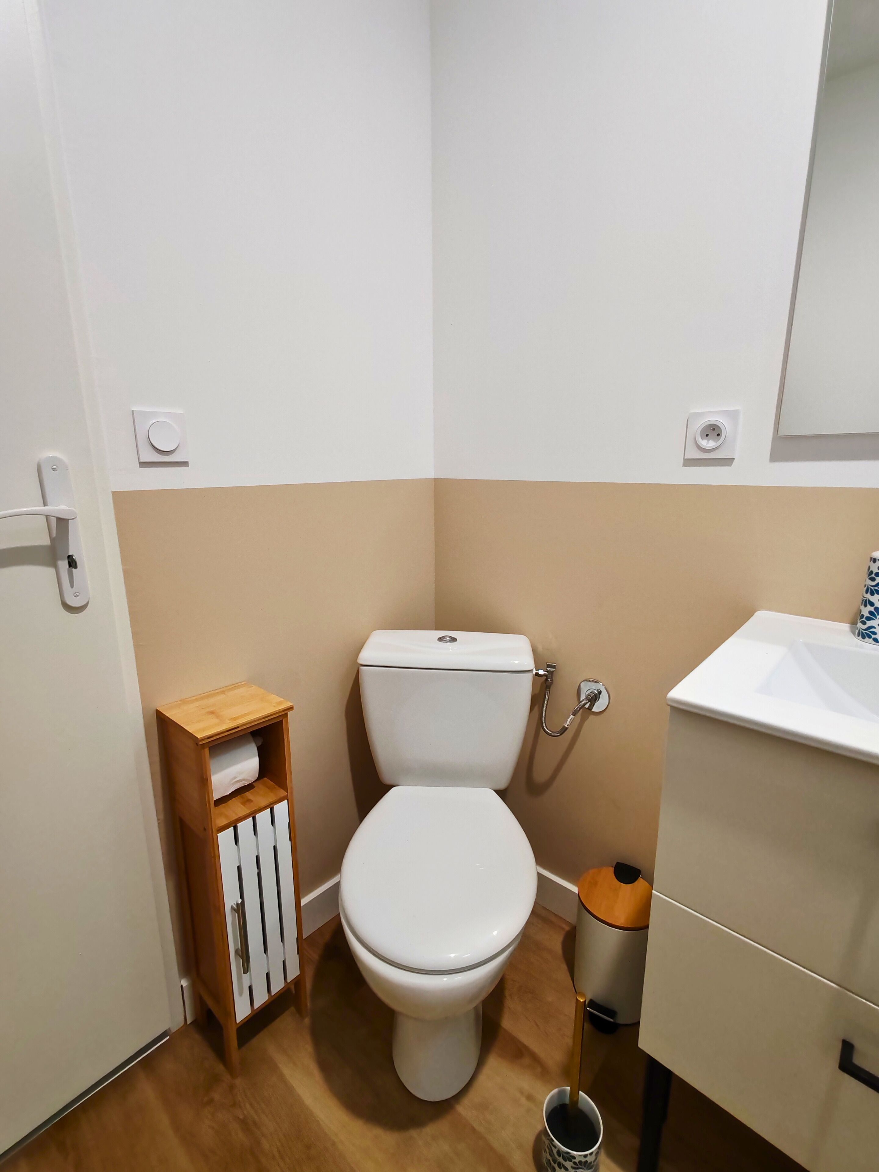A small, clean bathroom with a toilet, a wooden shelf with a towel, a sink, and a mirror.
