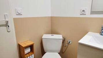A small, clean bathroom with a toilet, a wooden shelf with a towel, a sink, and a mirror.