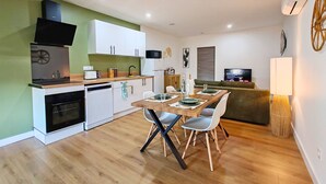 Una cucina funzionale con mobili bianchi, un forno a microonde e un piano cottura. C'è un'area pranzo con un tavolo di legno e sedie bianche. Un divano e una televisione si trovano nella zona soggiorno.