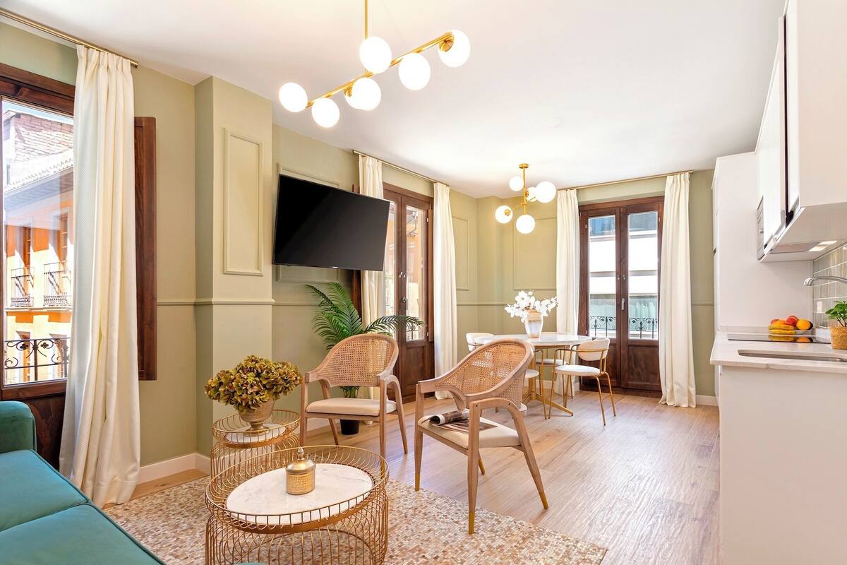 A modern living room with a flat-screen TV, wicker chairs, a round coffee table, and a dining area with a table and chairs.