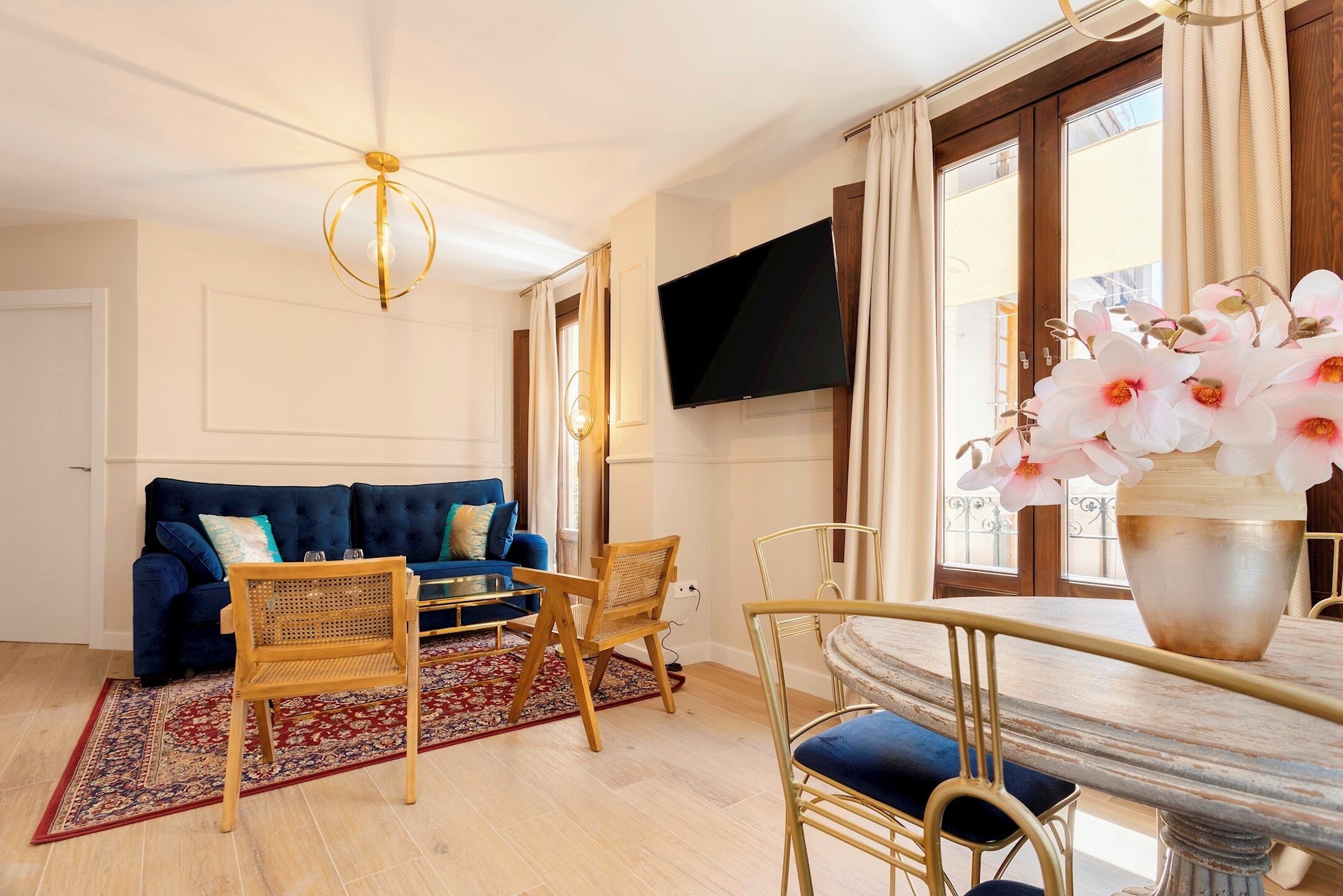 A living room with a blue sofa, wooden chairs, a dining table, and a TV mounted on the wall.