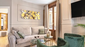 Ein modernes Wohnzimmer mit grauem Sofa, grünen Sesseln, einem Couchtisch und einer dekorativen Wandgestaltung.