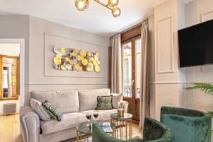 Uma sala de estar moderna com um sofá cinzento, poltronas verdes, uma mesa de centro e uma peça decorativa na parede.