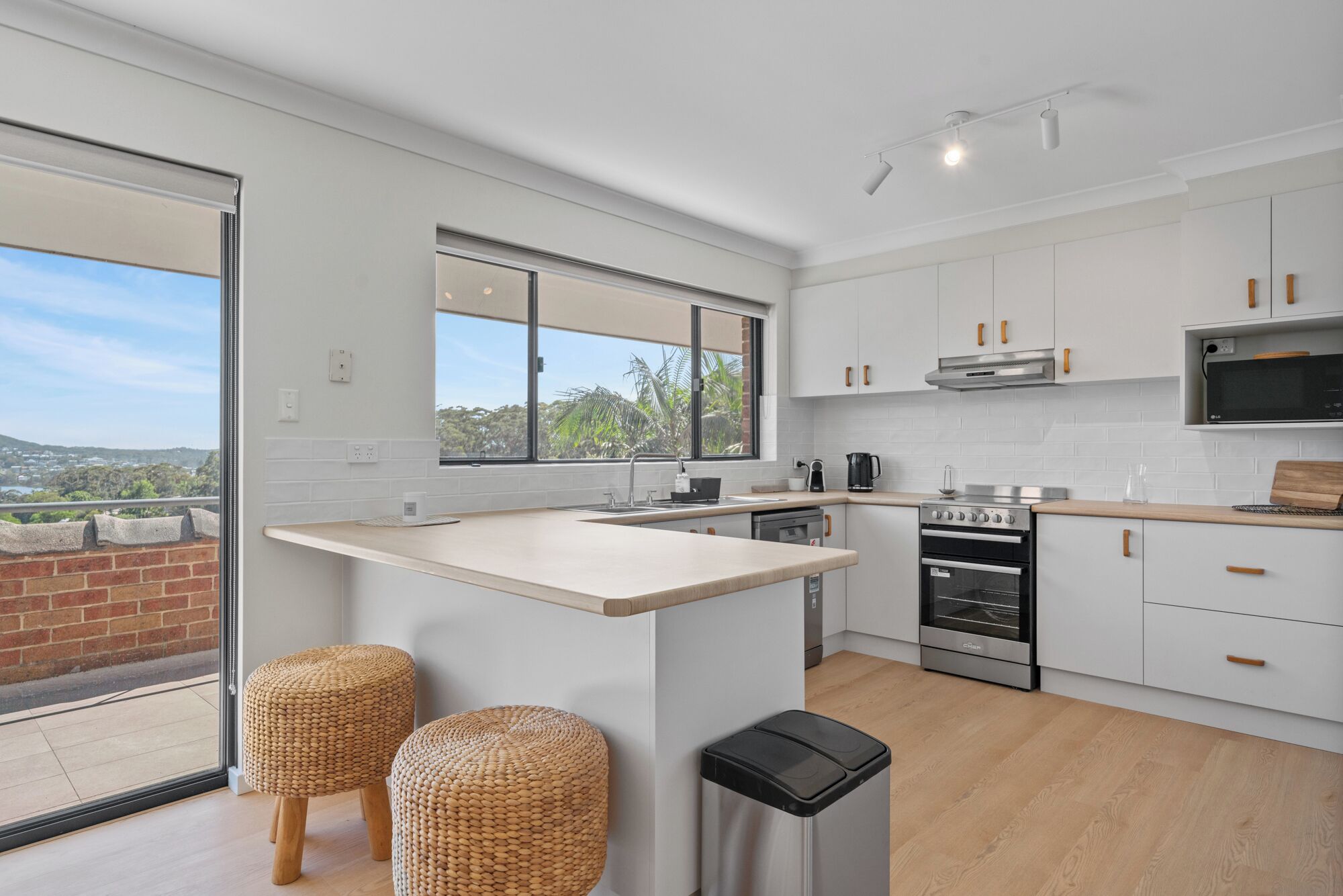 Une cuisine moderne avec des meubles blancs, un grand îlot central et une vue sur un balcon.