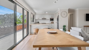 Een moderne keuken met witte kasten, een houten eettafel en een groot raam met uitzicht op een balkon.