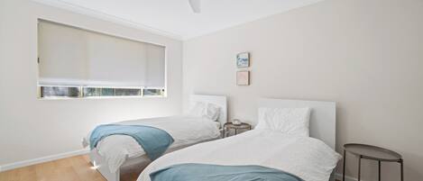 A bedroom with two beds, a ceiling fan, a small table, and a window with blinds.