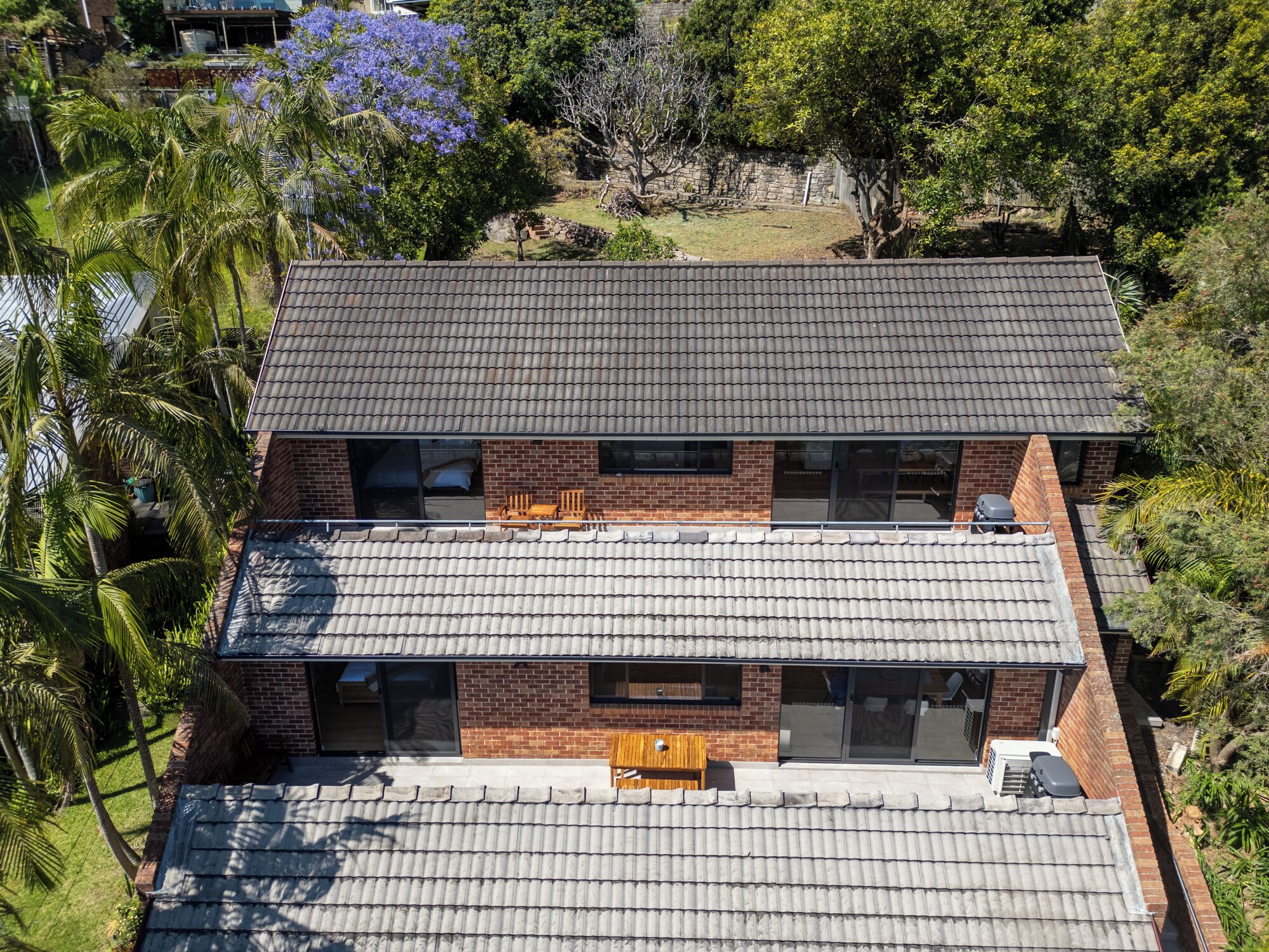 A two-story house with a tiled roof, brick walls, and a balcony with outdoor furniture.