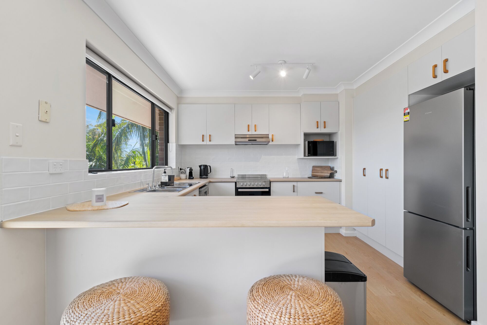 A modern kitchen with white cabinets, a stainless steel refrigerator, and a large island with stools.
