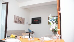 Hotellihuone, jossa on kahdelle katettu ruokapöytä, sänky, seinälle asennettu televisio ja ikkuna, jossa on verhot.