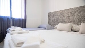 Hotellihuone, jossa on suuri sänky, pienempi sänky ja ikkuna, jossa on verhot.
