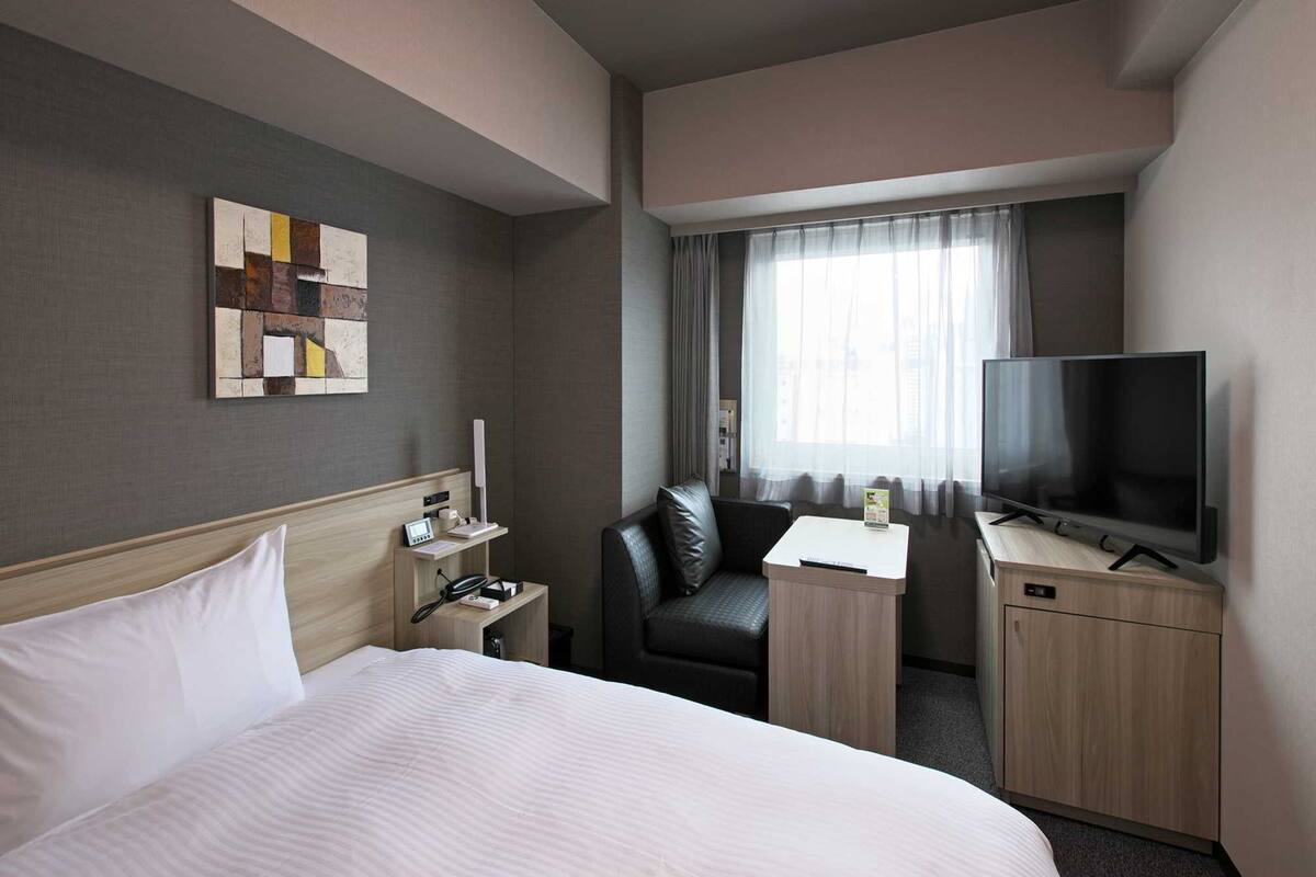 A hotel room with a bed, a desk, a TV, and a window with curtains.