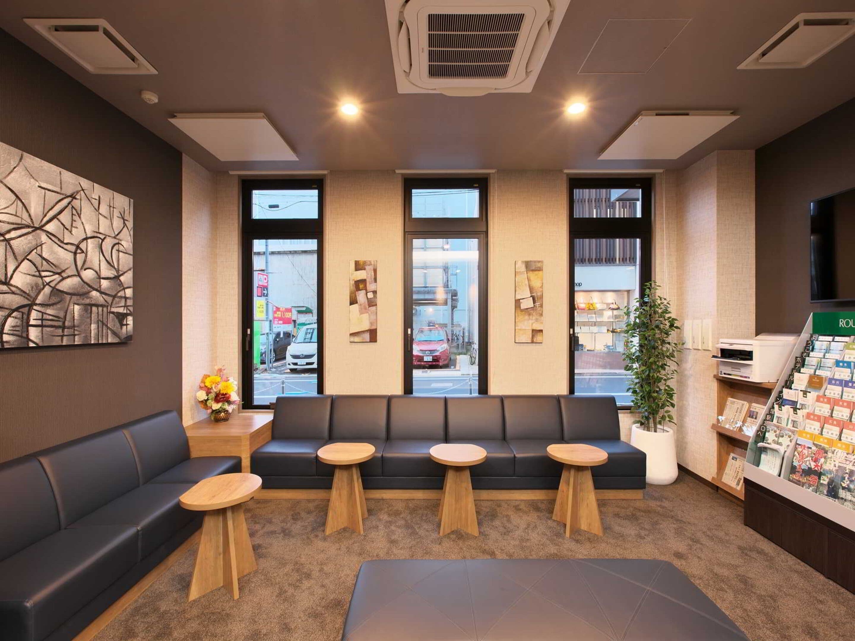 A modern reception area with a sofa, two round tables, and a large window with a view of the street.