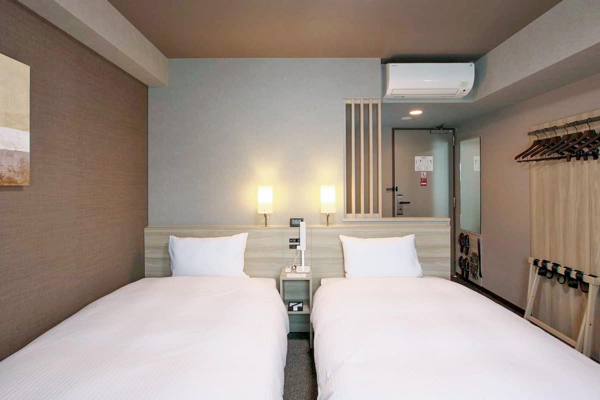 A hotel room with two beds, a nightstand, a wall-mounted air conditioner, and a mirror.