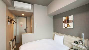Habitació d'hotel amb un llit, una taula de nit amb una làmpada, una obra d'art penjada a la paret i un aire condicionat fixat al sostre.