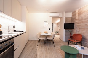 A modern kitchen with a dining area, a TV mounted on the wall, and a small table with a green stool.