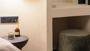 Ett modernt badrum med en rund spegel, en rund pall, ett litet bord med ett ljus och en doftspridare med doftstickor samt en väggmonterad lampa.