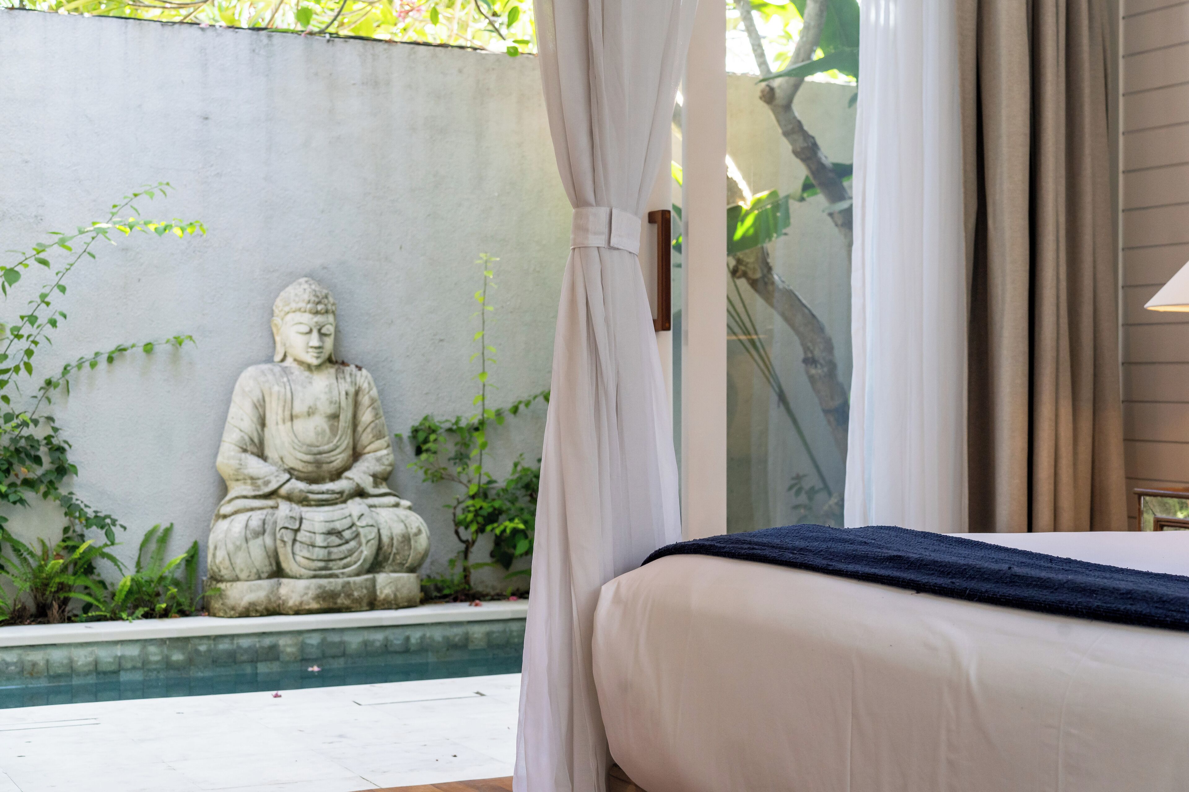 A room with a bed, a Buddha statue, a pool, and a view of greenery.