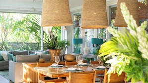 A sunlit dining area with a wooden table set for four, surrounded by chairs, and large woven pendant lights. - Villa Sunsara 2 (Canggu)