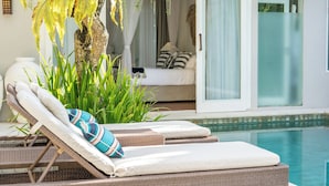A poolside lounge area with wicker chairs and cushions, a large potted plant, and a glimpse of a bedroom with a bed and curtains. - Villa Sunsara 2 (Canggu)