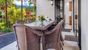 Een eethoek met een glazen tafel en rieten stoelen, met uitzicht op een tuin vol tropische planten en de zee.