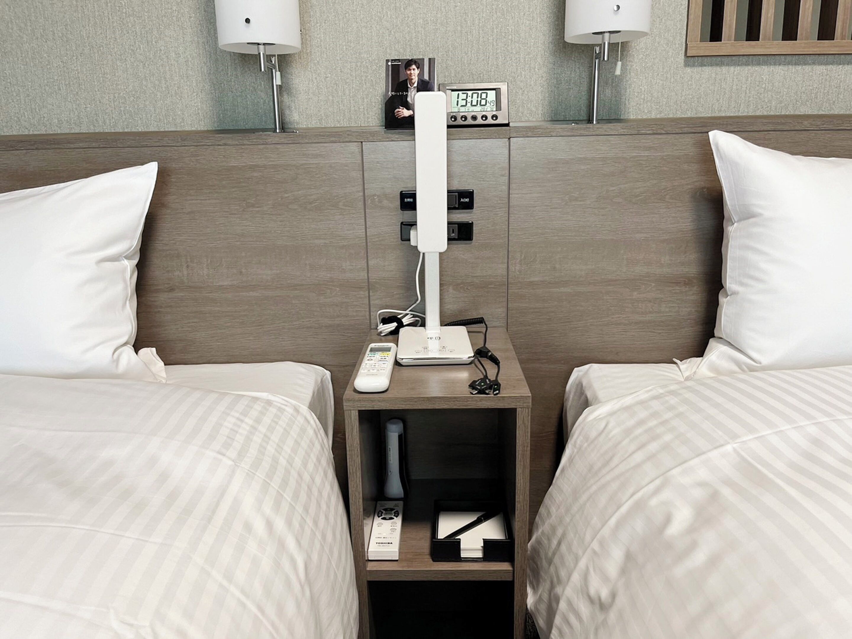 Habitación de hotel con dos camas, una mesita de noche con un reloj, un control remoto y una regleta de enchufes.