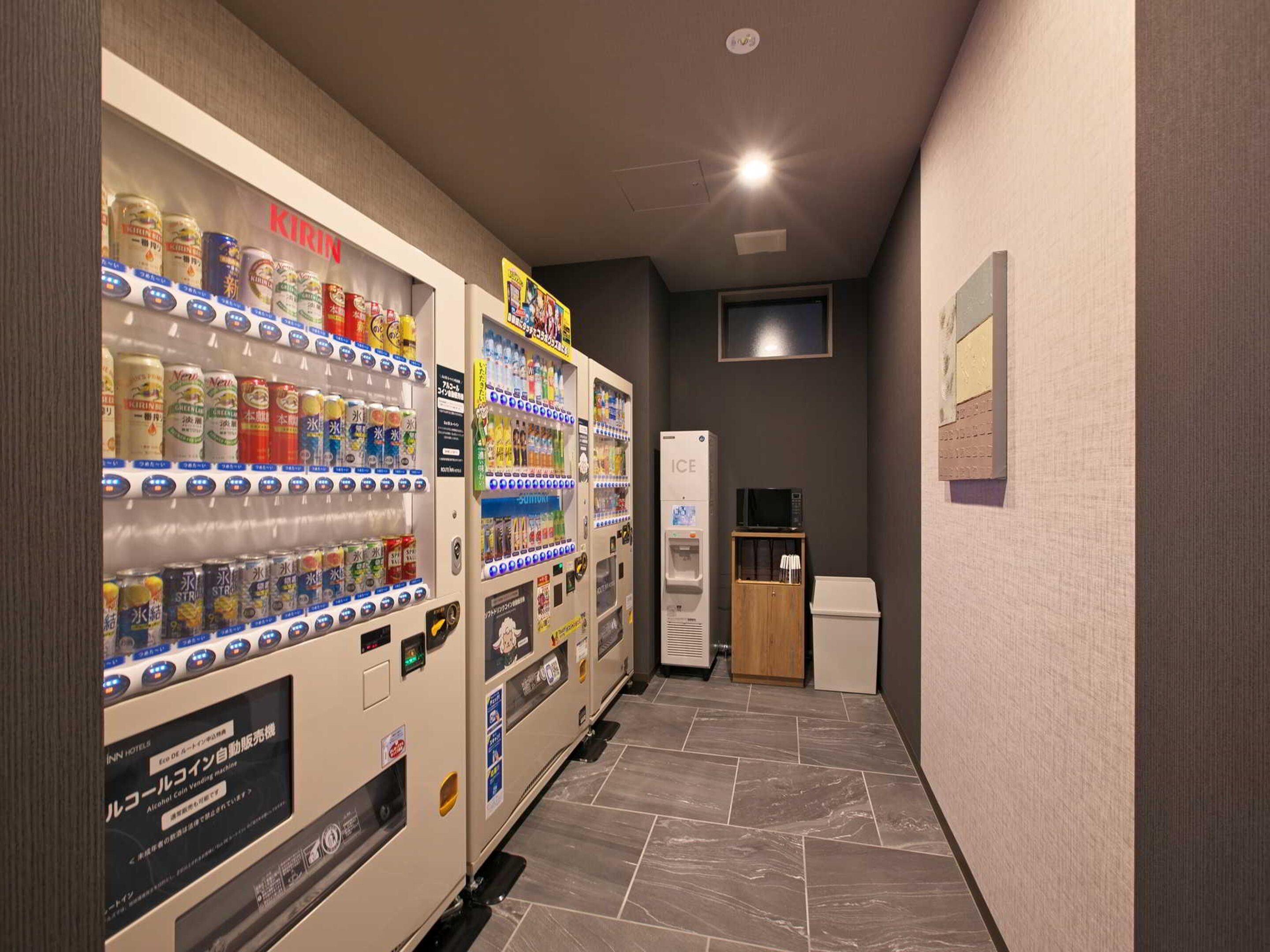 A hallway with vending machines stocked with beverages and snacks, a microwave, and a refrigerator.