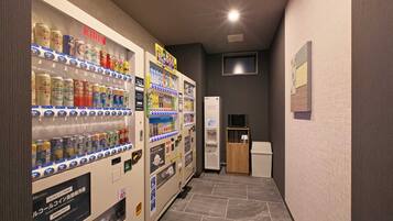 A hallway with vending machines stocked with beverages and snacks, a microwave, and a refrigerator.