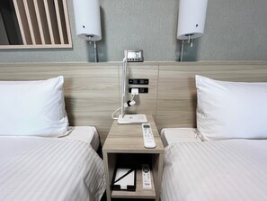 A hotel room with two beds, a nightstand with a digital clock, a remote control, and a power strip.