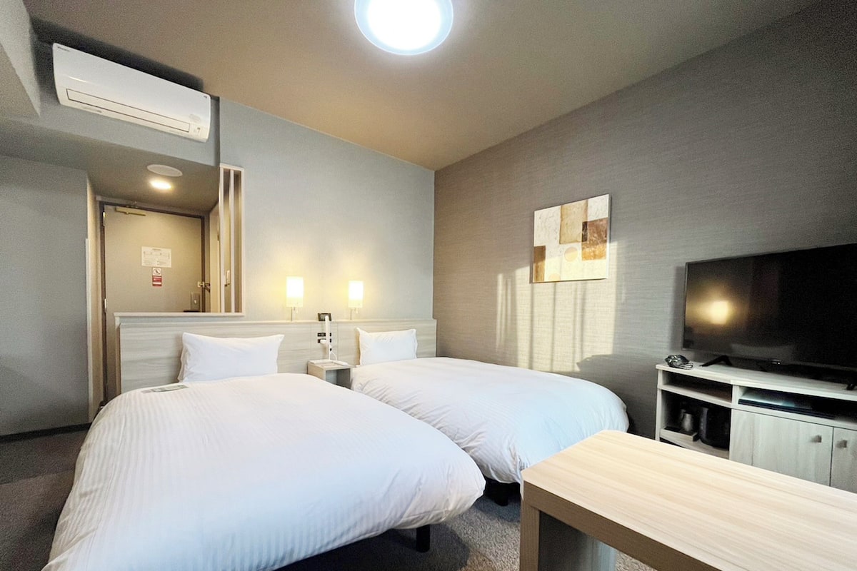 A hotel room with two beds, a TV, a desk, and a mirror.