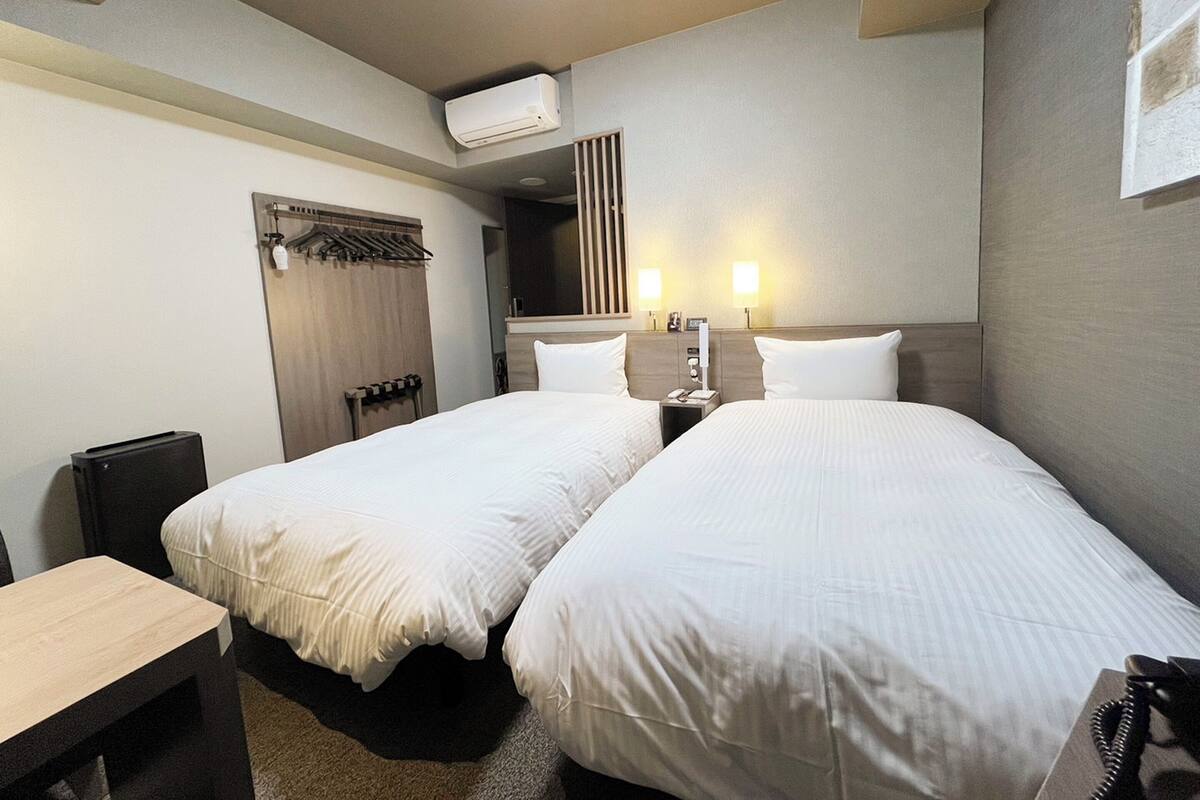 A hotel room with two beds, a desk, a wardrobe, and a mirror.