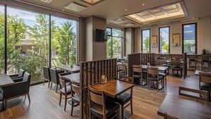A modern restaurant with wooden tables and chairs, large windows offering a view of the city, and a flat-screen TV mounted on the wall. - Hotel Route Inn Tonami Inter (Tonami)