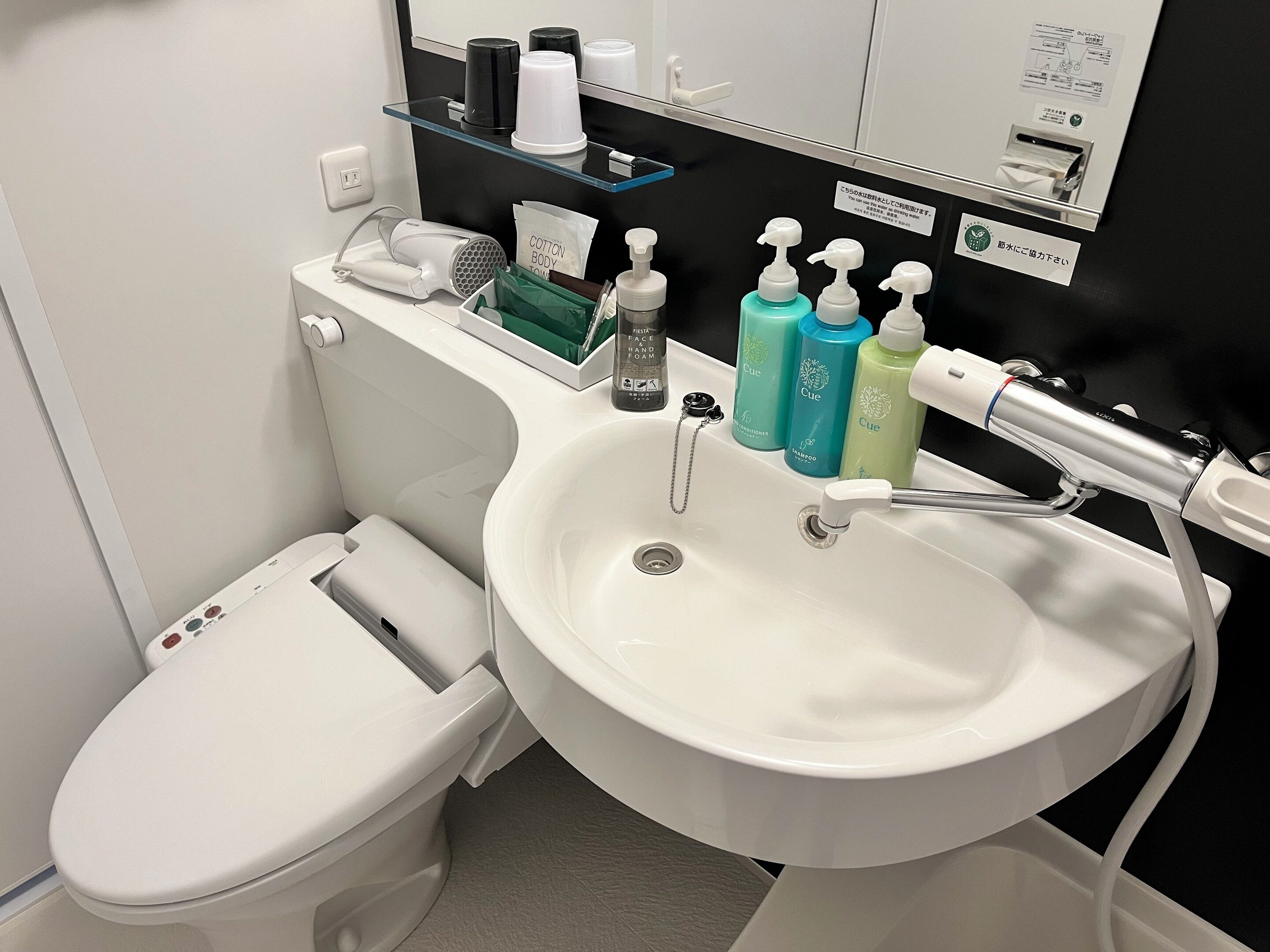 Un baño moderno con un inodoro blanco, un lavamanos grande con dispensadores de jabón y un secador de pelo en la encimera.