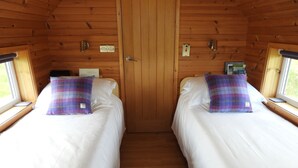 Een blokhut met twee bedden, elk met een geruit plaid en witte lakens. Houten wanden en een deur in het midden.