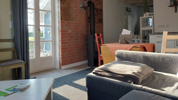 A living room with a brick wall, a sofa, a table, and a window with curtains. - Small, fine & rural (Pronstorf)