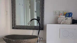 A bathroom with a stone sink, a black faucet, and a mirror with a black frame. There are toiletries on a shelf and a white cabinet with a circular design. - Small, fine & rural (Pronstorf)