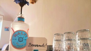 A bottle of Malfy gin, a small blue flower, and four clear glasses on a wooden surface. - Cozy apartment for families and groups of friends 5 minutes from downtown (Torino)