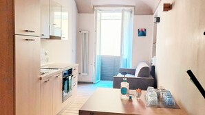 A modern kitchen with a wooden table, a chair, and a view to a living area with a sofa and a window. - Cozy apartment for families and groups of friends 5 minutes from downtown (Torino)