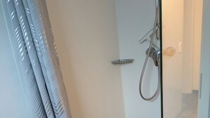 Una ducha con cerramiento de vidrio, un cabezal de ducha manual, un perchero y una cortina de baño.