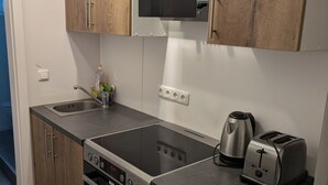 Una cocina compacta con armarios de madera, una estufa de acero inoxidable, un tostador y una tetera.