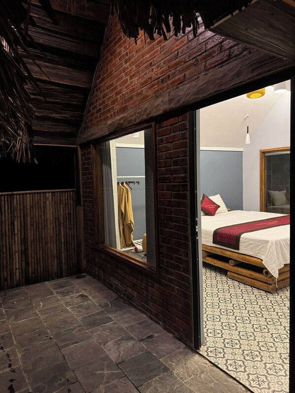 A room with a brick wall, a bed with a red blanket, a window with a yellow towel, and a patterned floor. - Tam Coc Golden Fields Homestay (Nam Hoa Lu)