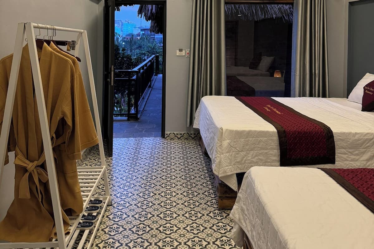 Ein Hotelzimmer mit zwei Betten, einem Schrank, einer Pendelleuchte und Blick ins Freie.