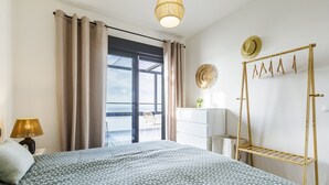 A bedroom with a bed, curtains, a hanging light fixture, a dresser, a hat rack, and a view through a window. - A&N atico dimo terraza del Mar (Algarrobo Costa)