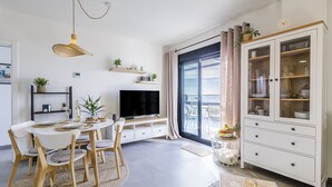 A modern living room with a dining area, a TV, and a large window with curtains. - A&N atico dimo terraza del Mar (Algarrobo Costa)