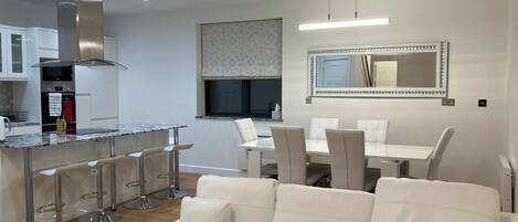 A modern kitchen with a central island, bar stools, and a dining area with a white table and chairs.