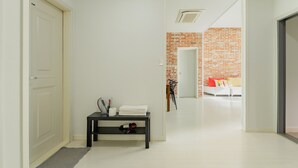 A hallway with a white door, a black console table with towels and a hairdryer, and a brick wall with a mirror and a white sofa in the background. - Jeju Pureunbada Pet Dokchae Pension (Jeju City)